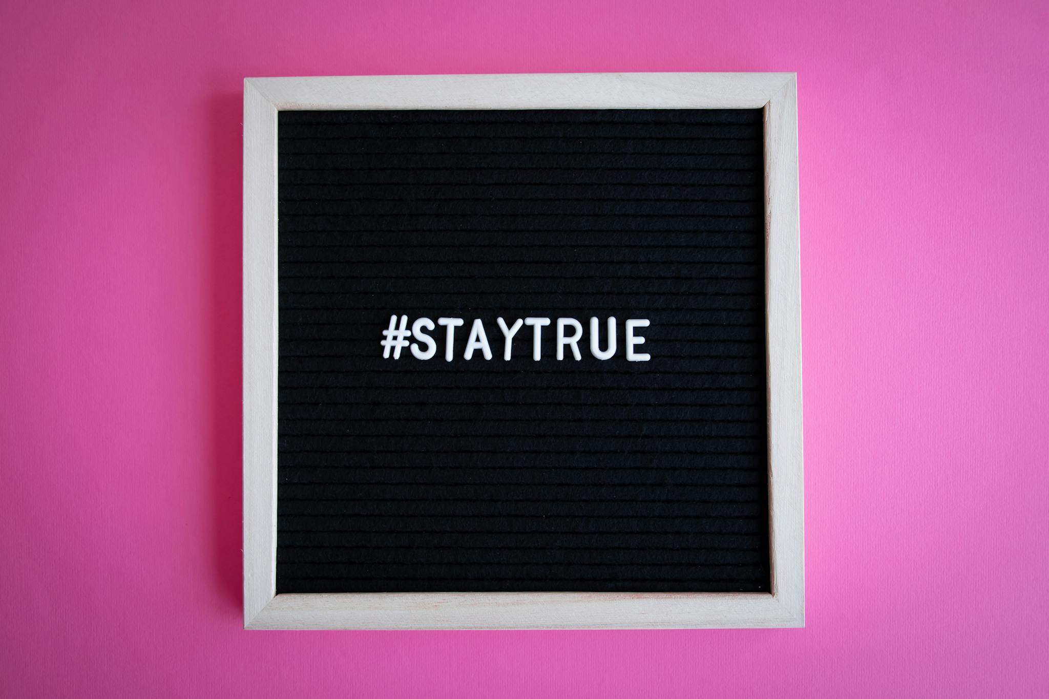 Black letter board with motivational text '#StayTrue' on pink background.