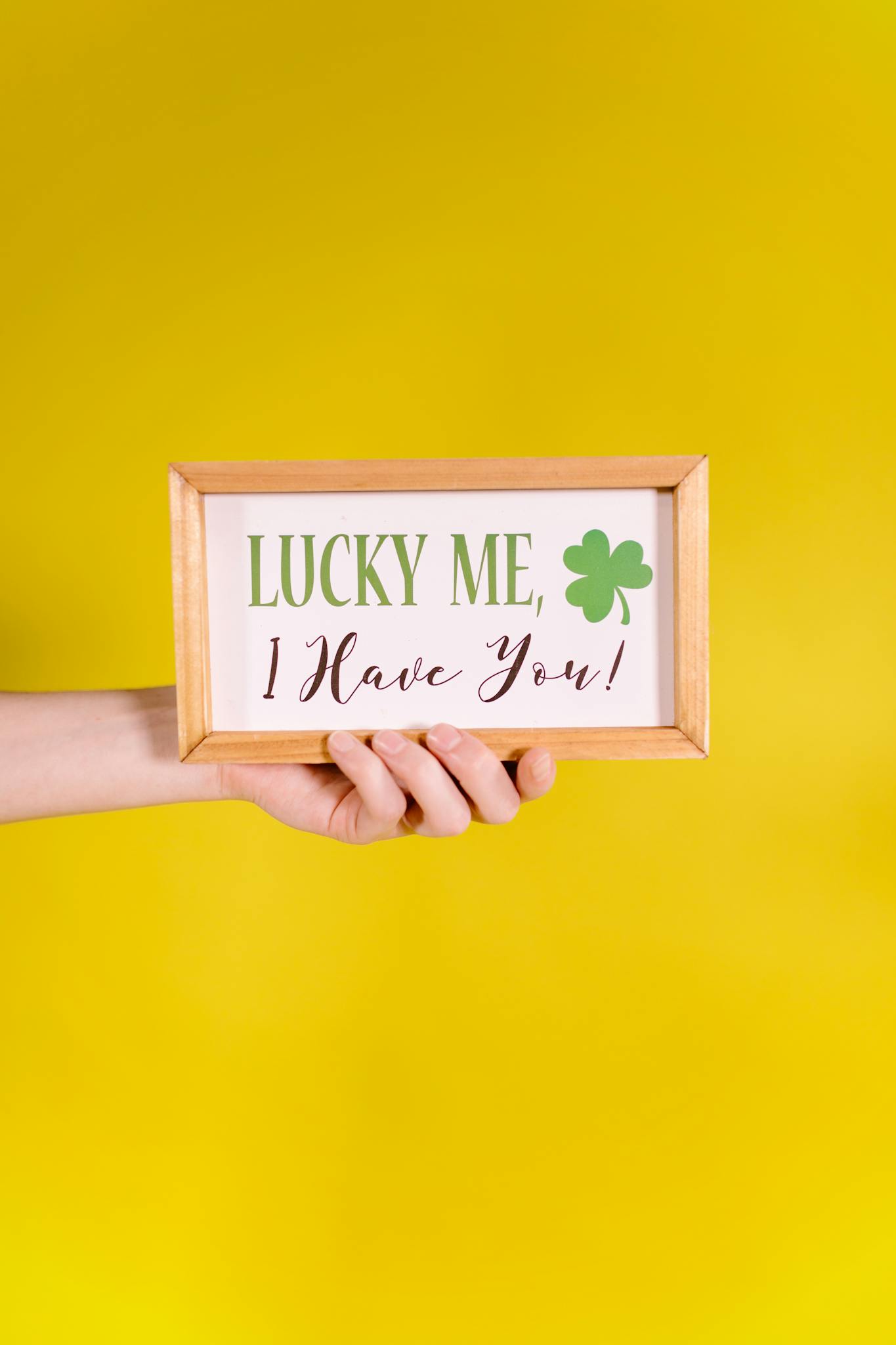 A hand holds a framed quote 'Lucky Me, I Have You!' against a bright yellow background.