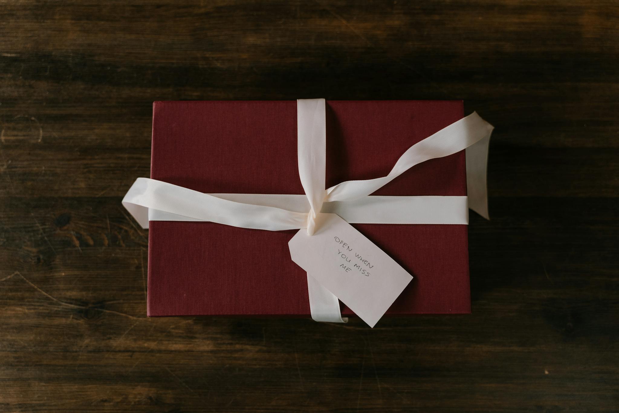Red gift box with white ribbon and handwritten tag on rustic wooden background.